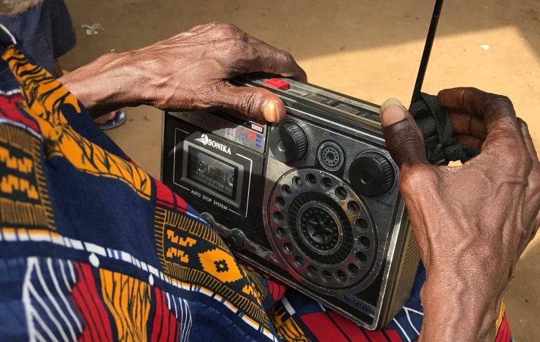 An elderly African woman listening to an old radio.