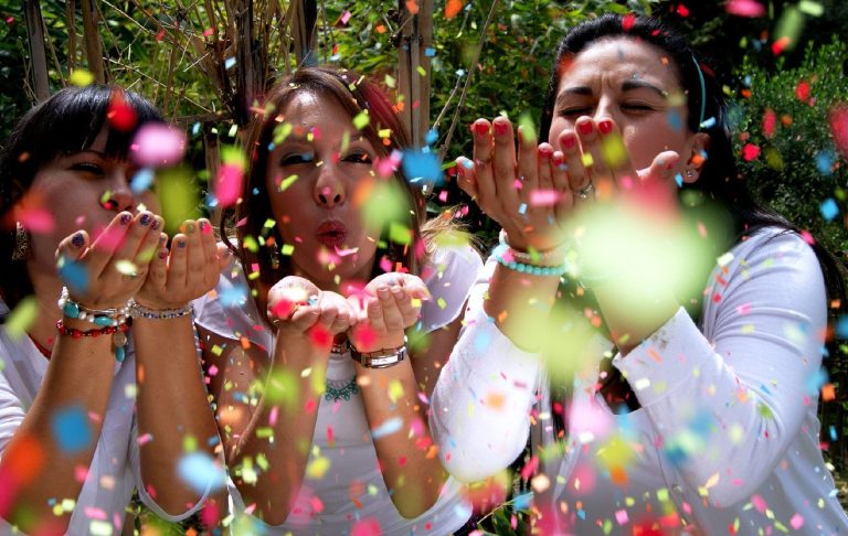 Three women celebrate social change blowing coloured coloured confetti